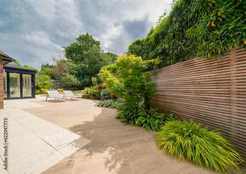 View of stylish, luxury, designer patio and garden with loungers and plants on sunny, summer day.