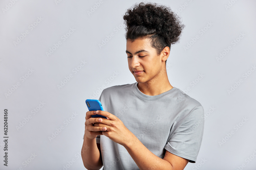Studio portrait of a young handsome brunette man with curly hair holding a smartphone in his hands. A swarthy guy typing a message on a cell phone. Modern lifestyle. Isolated on a gray background. Studio portrait of a young handsome brunette man with curly hair holding a smartphone in his hands. A swarthy guy typing a message on a cell phone. Modern lifestyle. Isolated on a gray background.