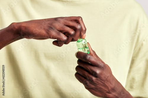 Close-up of a young black man's hands holding a small bottle of medicated skin care serum or moisturizing balm. Use of cosmetics helps to keep skin young and healthy. Men's skin care concept.