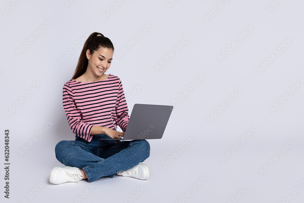 Happy young woman digital nomad using laptop, grey background Happy young woman digital nomad using laptop, grey background