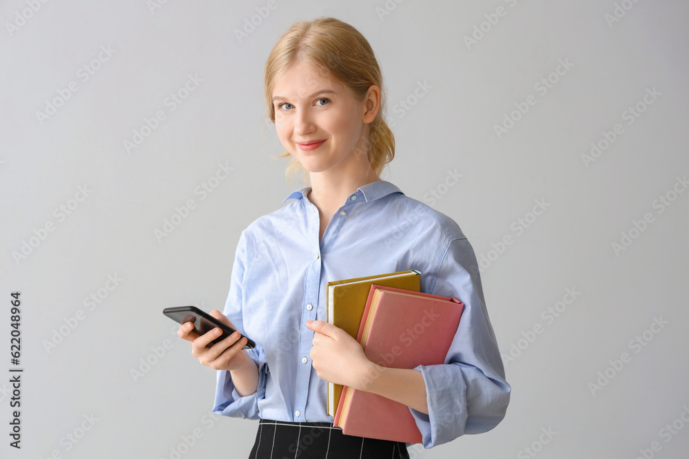Female student with books using mobile phone on grey background Female student with books using mobile phone on grey background