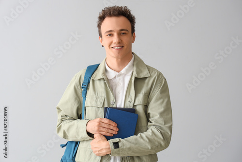 Male student with backpack and books on grey background