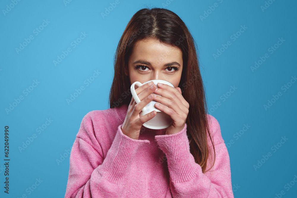 Close up portrait of young hispanic brunette woman looking at camera and drinking hot beverage from cup, isolated on blue background. People, emotions concept Close up portrait of young hispanic brunette woman looking at camera and drinking hot beverage from cup, isolated on blue background. People, emotions concept