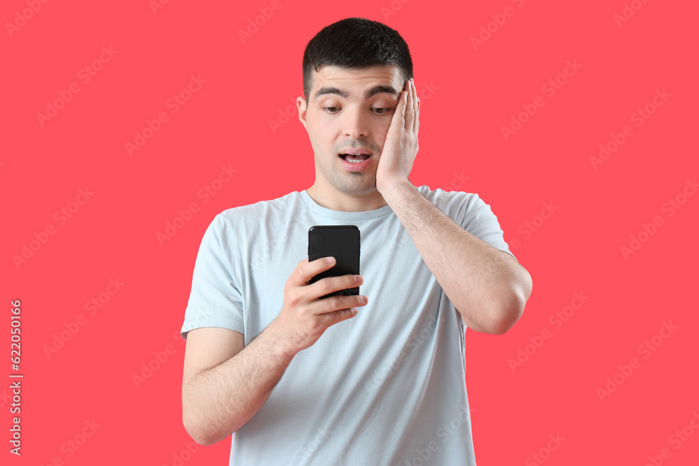 Surprised young man with smartphone on red background Surprised young man with smartphone on red background