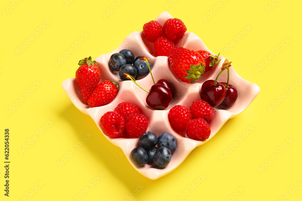 Ice cube tray with different fresh berries on yellow background Ice cube tray with different fresh berries on yellow background
