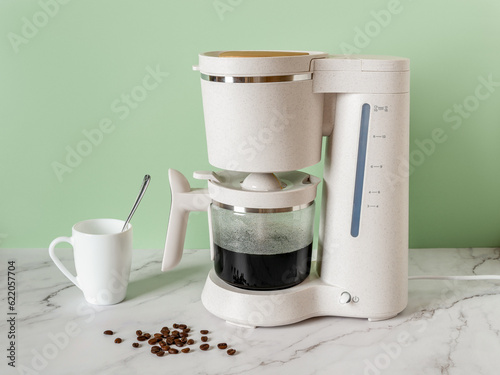 Automatic drip coffee maker brews a morning drink. Electric coffee machine filling glass pot with hot black coffee on a marble countertop at home. Household appliances. Breakfast concept.
