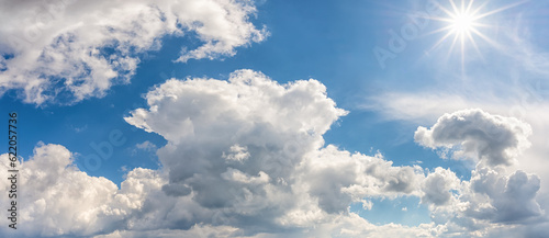 Bright sun shines high in a blue summer sky panorama. Wide shot of spring sky with white clouds on a sunny midday. Weather forecasting  touris and travel concept. Sky only.