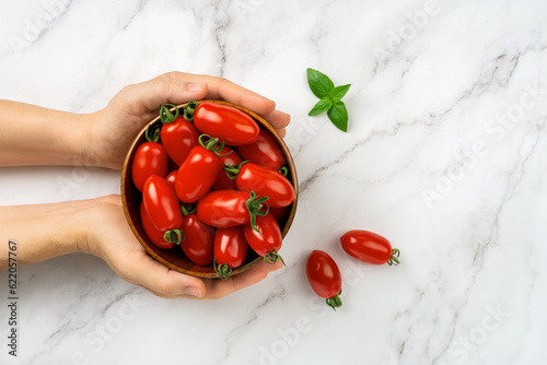 Bowl of fresh Ornela cherry tomatoes in a woman hands over white marble background. Female hands hold bowl of red ripe small tomatoes. Organic vegetables, healthy eating, harvest concept. photo