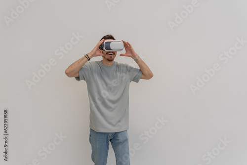 Futuristic man wearing virtual reality glasses interacts with the air in an isolated gray background. © Minet