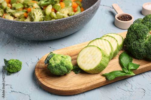 Wooden board with different fresh vegetables on grey background