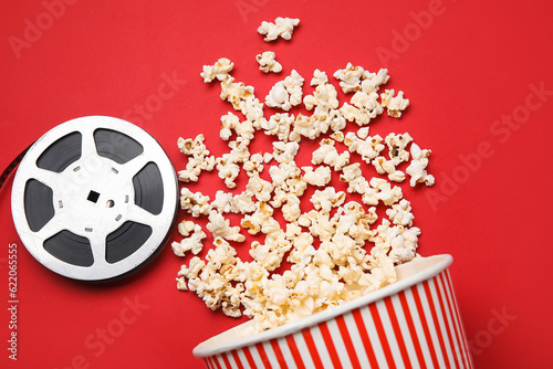 Bucket with tasty popcorn and film reel on red background