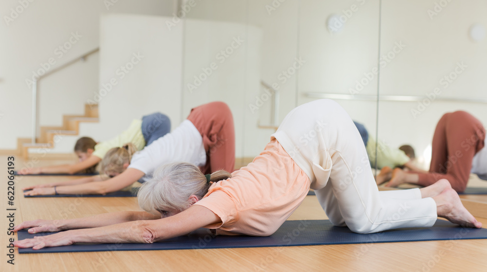 Senior woman exercising melting heart yoga pose during group training.