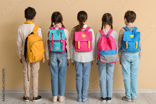 Little pupils with backpacks near beige wall, back view