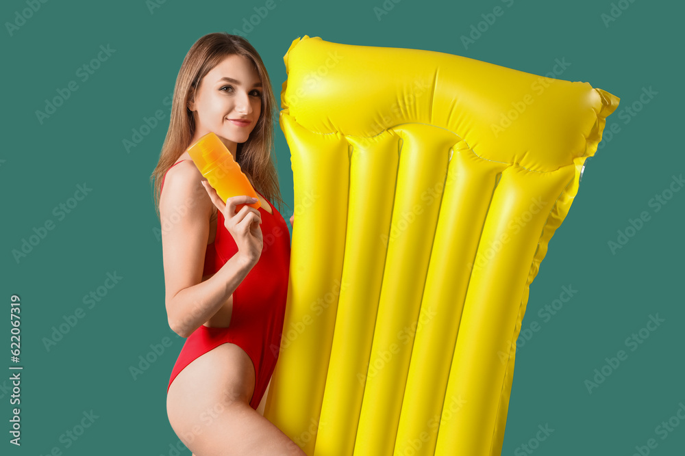 Obraz premium Young woman with sunscreen cream and inflatable mattress on green background