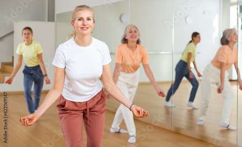 Positive woman learning jazz style dance during group training in studio.
