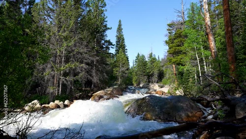 a powerful rushing river from snow melt flows in the mountains with sound audio of the water streaming by and blue skies above