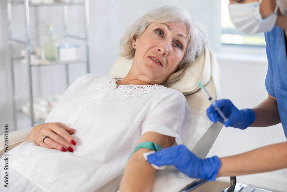 Obraz premium Old gray haired lady laying at examination couch before having intravenously injection by nurse
