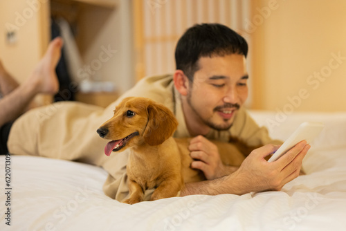 ホテルのベッドで飼い犬とスマートフォンを見る男性