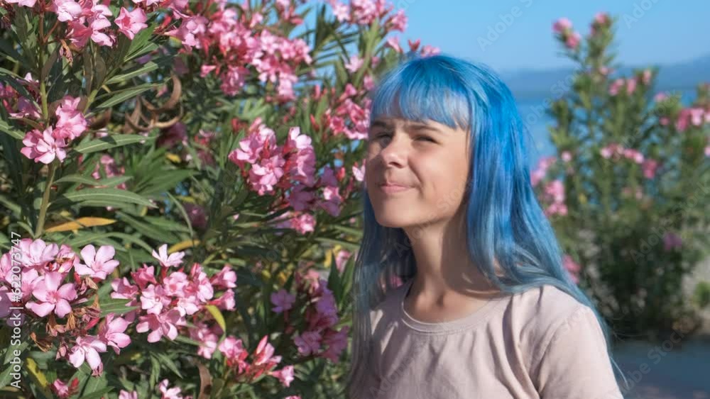 A teenager scratches his nose from pollen. A girl with blue hair near a flower bush scratches her itchy nose.