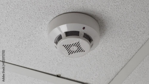 Smoke detector mounted on a suspended ceiling with blinking red LED.
