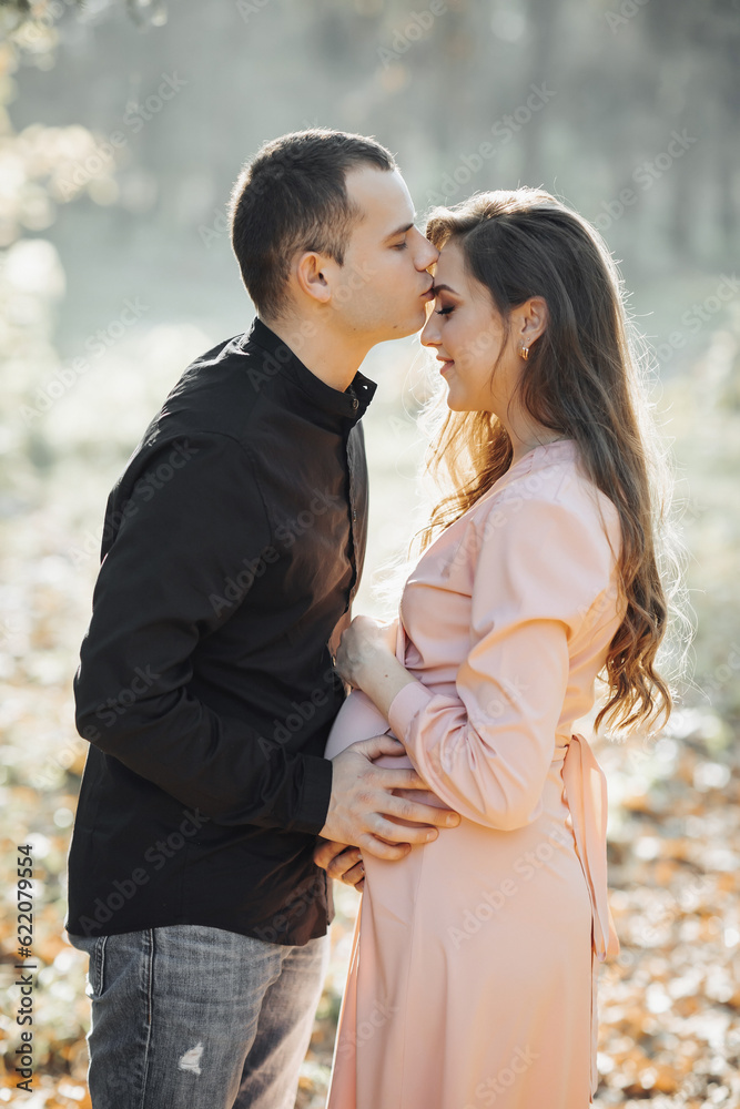 A man and his pregnant wife hug and kiss in the forest at sunset. Happy family concept. A man and his pregnant wife hug and kiss in the forest at sunset. Happy family concept.