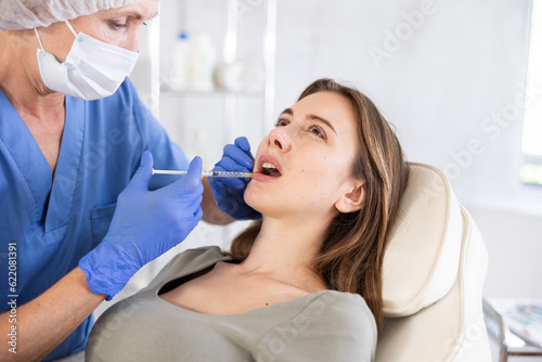 Professional doctor in scrub giving calm female patient lip fillers