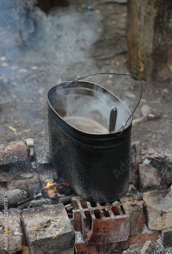 Tea is brewed in a pot on a fire in the forest. Bonfire. camping pot. Cooking food and drinks on a fire, picnic. Travel equipment.