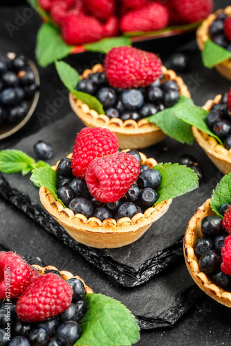 Tartlets with blueberries, raspberries and mint leafs on a black slate background