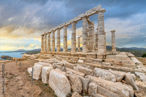 Fotografie, Obraz The Temple of Poseidon, an ancient Greek temple on Cape Sounion, Greece, dedicated to the god Poseidon, with the Aegean sea and coastline seen under early sunset dramatic skies