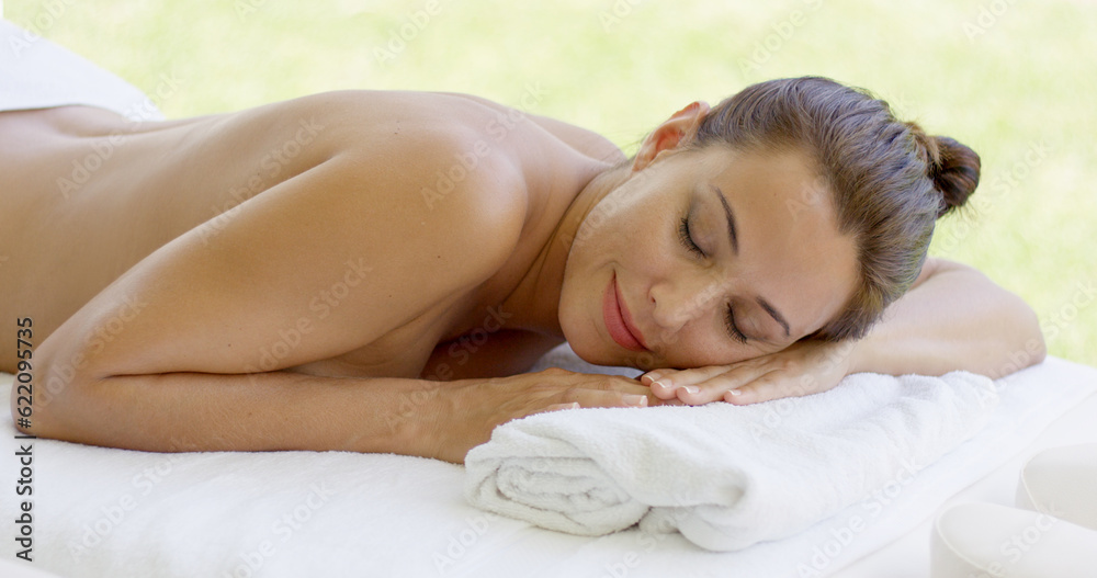 Woman relaxing on spa table on outdoor patio closes her eyes and smiles to herself Woman relaxing on spa table on outdoor patio closes her eyes and smiles to herself
