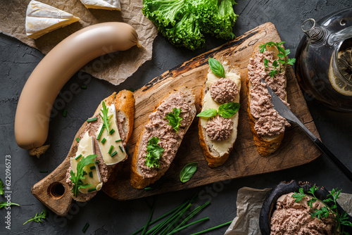 Delicious sandwiches with pate, cheese, greens, spices on cutting board with onion on dark background. Meat food, top view