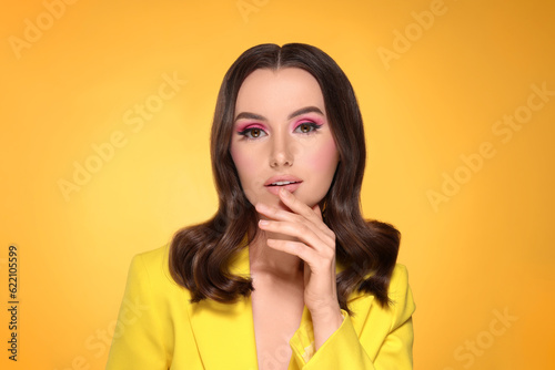 Portrait of beautiful young woman with makeup and gorgeous hair styling on yellow background