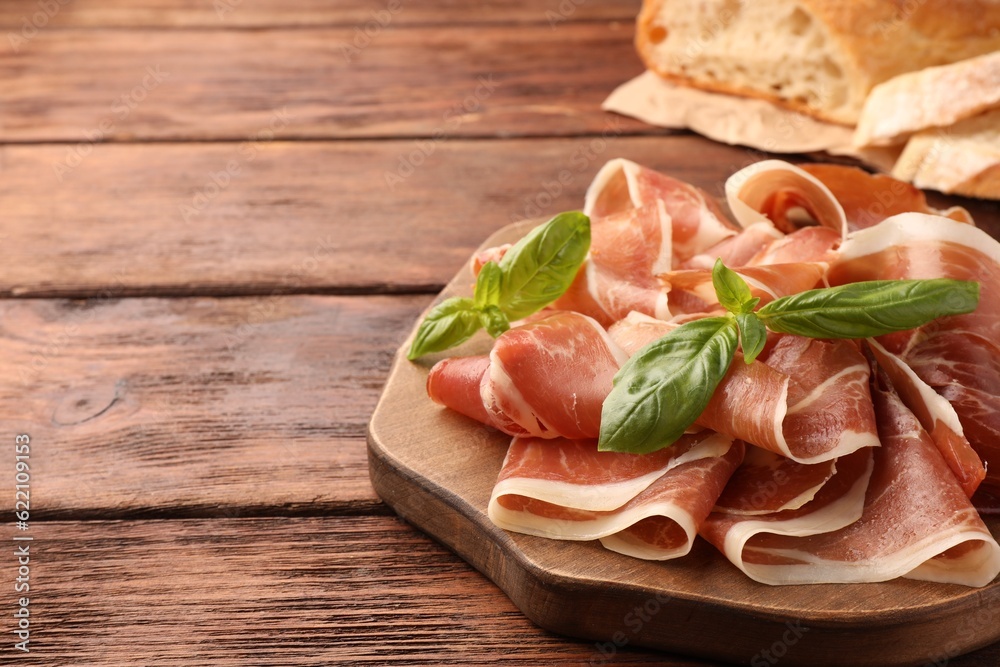 Slices of tasty cured ham and basil on wooden table, closeup. Space for text Slices of tasty cured ham and basil on wooden table, closeup. Space for text