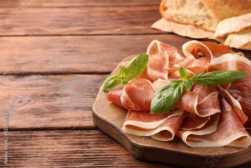 Slices of tasty cured ham and basil on wooden table, closeup. Space for text