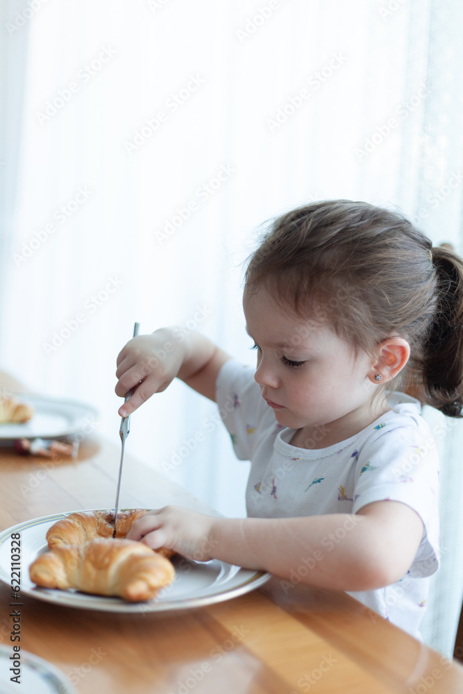 Cute little girl eating croissant in the morning at home Cute little girl eating croissant in the morning at home