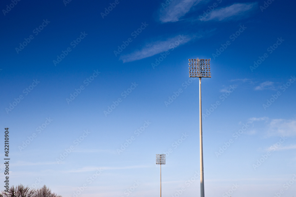 Stadium floodlights, used to lit a sports arena, also called reflectors or projectors, during a sunny afternoon. These are high consumers of power and energy. Stadium floodlights, used to lit a sports arena, also called reflectors or projectors, during a sunny afternoon. These are high consumers of power and energy.