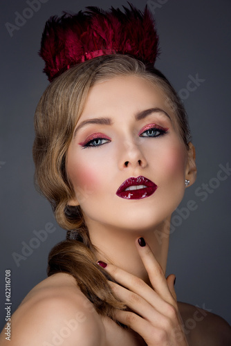 Beautiful girl with red feather crown and bright makeup. Closeup beauty shot. Over dark background.