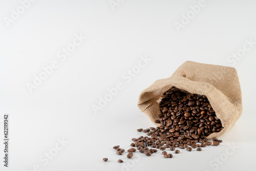 Roasted coffee beans falling in a burlap sack. Sackcloth bag with coffee beans, isolated on white background. Coffee export.