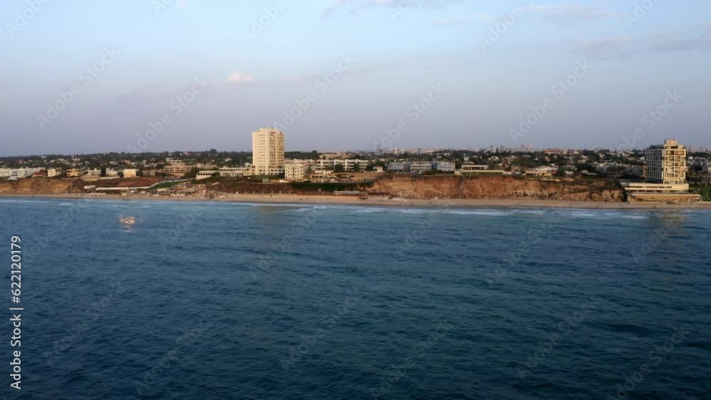 Aerial Shot Of Beach Near Buildings In City Against Cloudy Sky, Drone Flying Forward Over Sea At Sunset - Herzeliya, Israel Aerial Shot Of Beach Near Buildings In City Against Cloudy Sky, Drone Flying Forward Over Sea At Sunset - Herzeliya, Israel