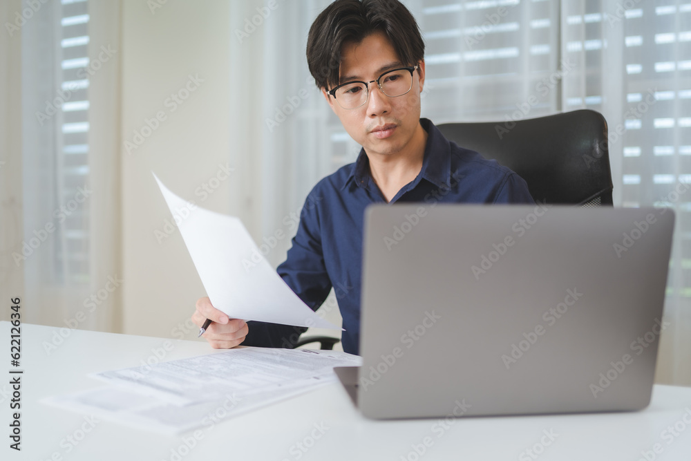 Asian businessman holds business contract agreement for check and manage business contract document with laptop. Investor analyzing business document paperwork for decide to investment on business Asian businessman holds business contract agreement for check and manage business contract document with laptop. Investor analyzing business document paperwork for decide to investment on business