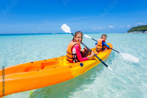 Kids enjoying paddling in orange kayak at tropical ocean water during summer vacation