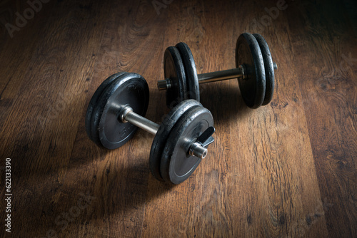 Black barbell weights on dark hardwood floor, weightlifting training concept.