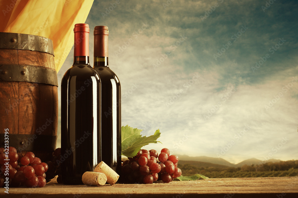 Obraz premium Red wine bottles with barrel and grapes, vineyard on background