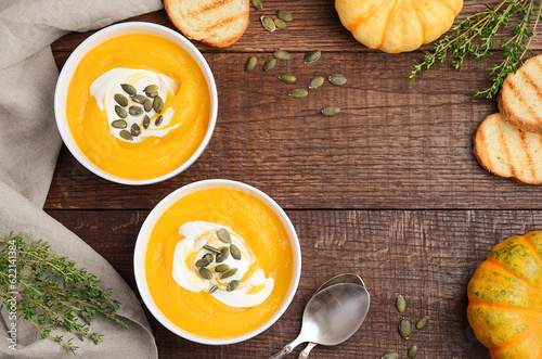 Pumpkin cream soup with cream and pumpkin seeds on wooden background, top view, copy space