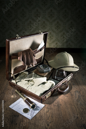 Open leather suitcase with adventurer vintage equipment, including pith hat and brass telescope.