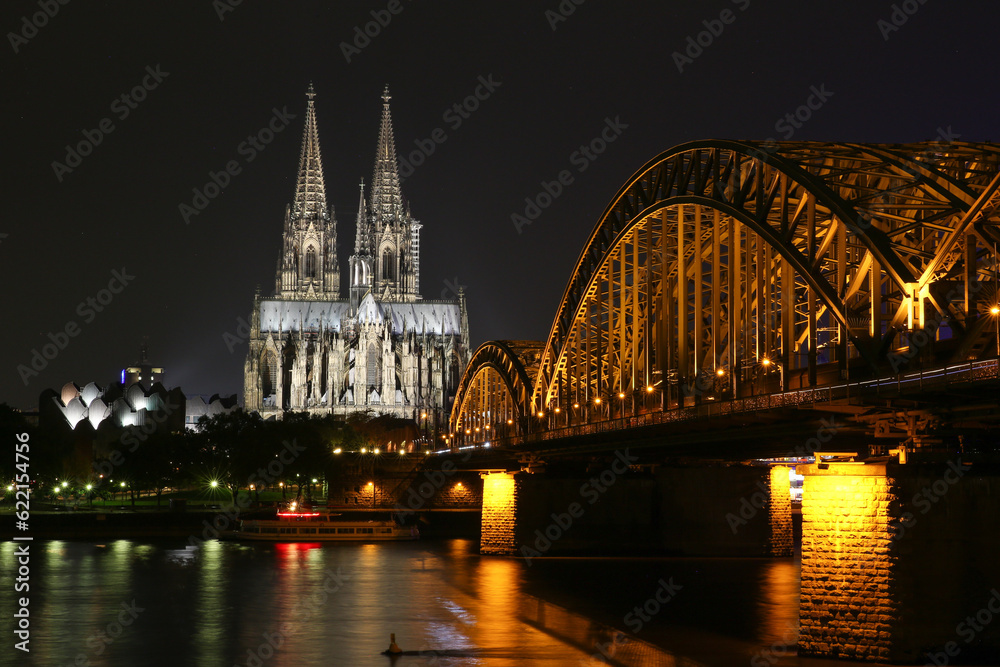 Fototapeta premium Cologne, Germany - October 16, 2013. Beautiful night view of the Cologne Cathedral and the bridge over the river. Golden lights reflected in the water. And no one around.