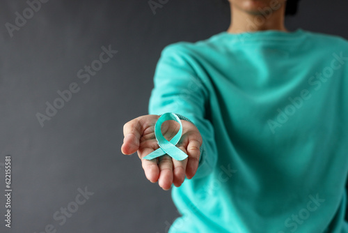 Female in green sweater holding and showing green organ transplant awareness ribbon to the camera, symbol of fight against disease. World lymphoma awareness day.  photo