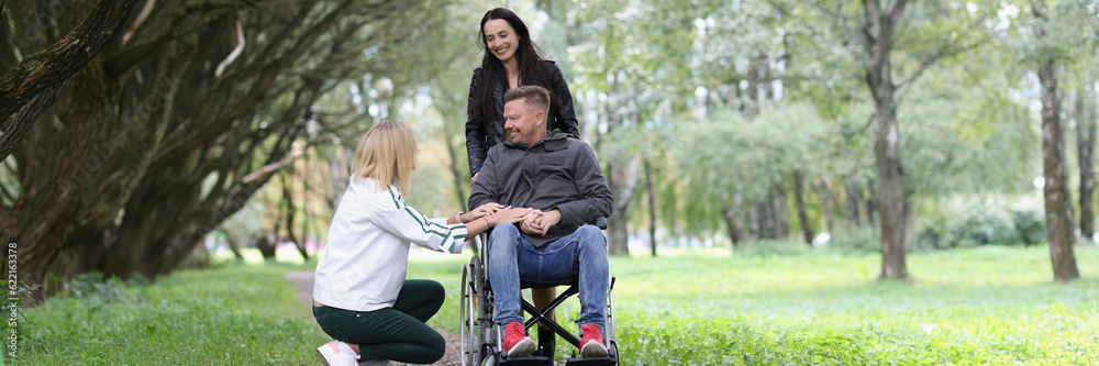 Smiling man in wheelchair and two women have fun in the park