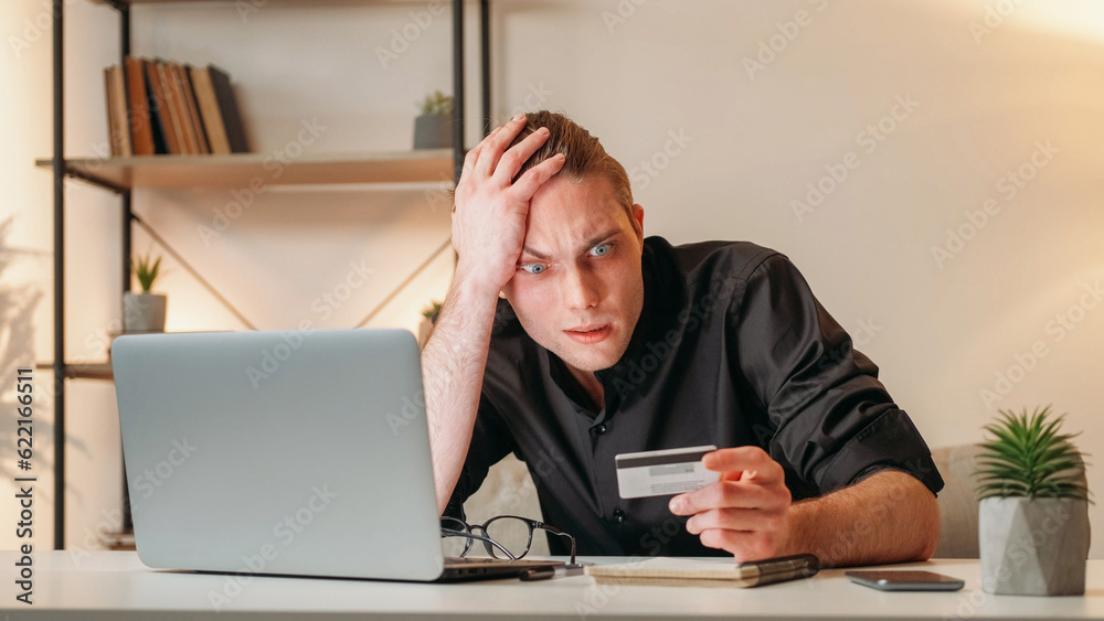 Bank scam. Financial fraud. Money transaction risk. Frustrated overwhelmed stressed business man with credit card laptop at workplace interior with free space. Bank scam. Financial fraud. Money transaction risk. Frustrated overwhelmed stressed business man with credit card laptop at workplace interior with free space.