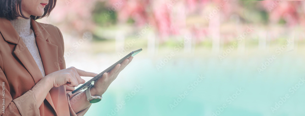 Banner Asian woman hands using digital tablet shopping online at lake autumn park. Panorama Female hands pointing smart tablet use mobile app work travel. Asian woman Smart technology with copy space